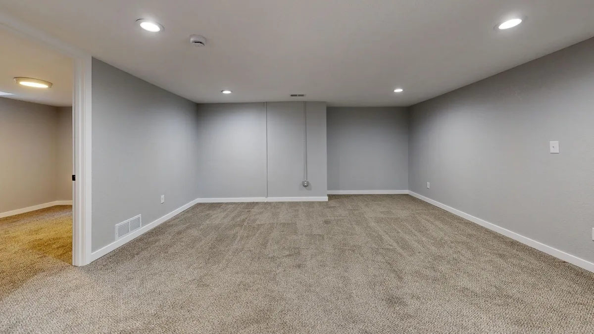 Finished basement renovation showing modern living space with built-in shelving, comfortable seating, and proper lighting